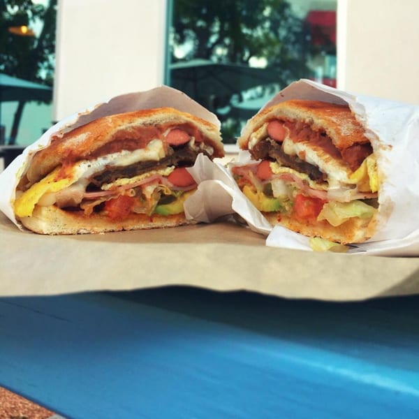 A Mexican torta, cut in half, revealing layers of meat, hot dogs, egg, and vegetables.