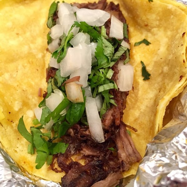 Close-up of a Papalote Taco House taco with shredded meat, diced onions, and cilantro.