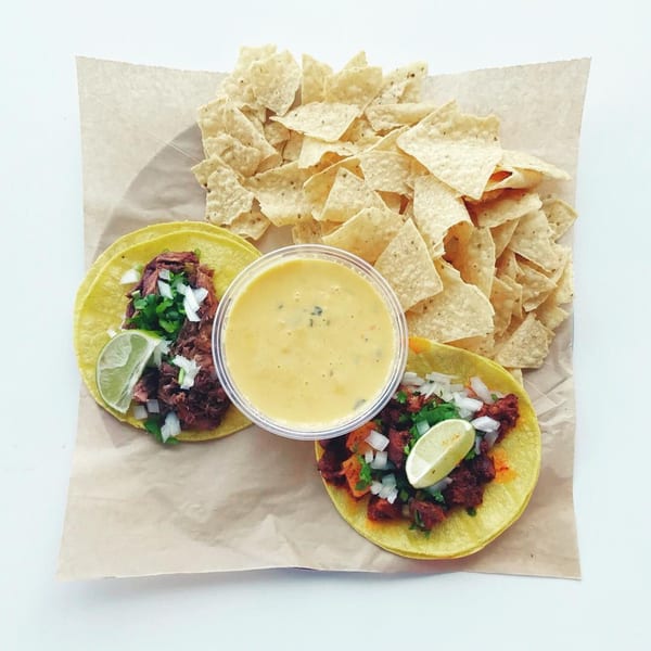 Two Papalote Taco House tacos with lime, onions, cilantro, a side of queso, and tortilla chips.